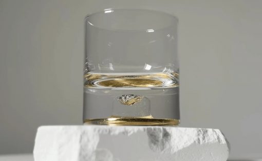 Clear glass tumbler with a small amount of amber liquid, resting on a white rough stone block on a white surface.