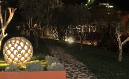 Night garden with illuminated perforated sphere sculptures along a stone path at night.