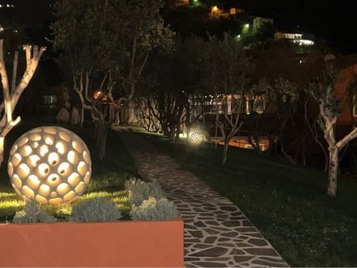 Night garden with illuminated perforated sphere sculptures along a stone path at night.