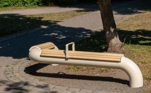 Curved white pipe bench with wooden slats beside a tree in a park setting