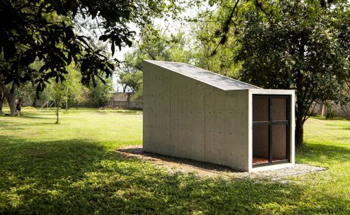 Concrete shed with a sloped roof in a green park, surrounded by trees.