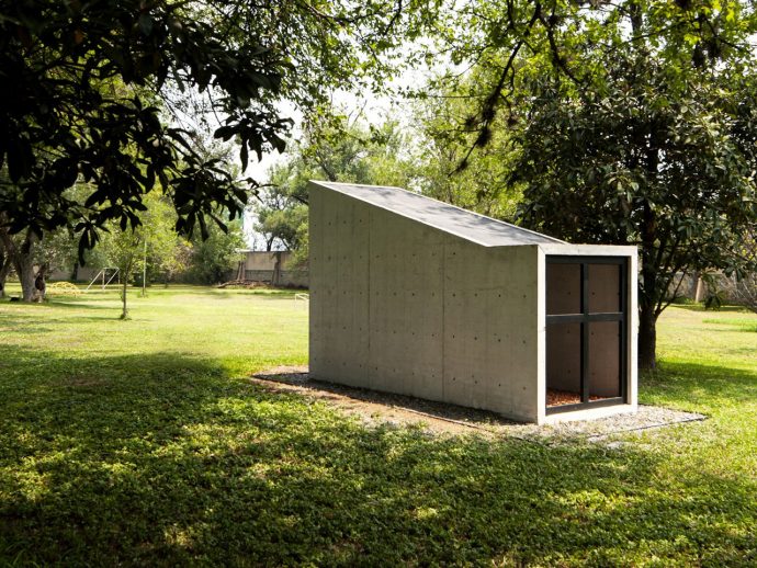 Concrete shed with a sloped roof in a green park, surrounded by trees.