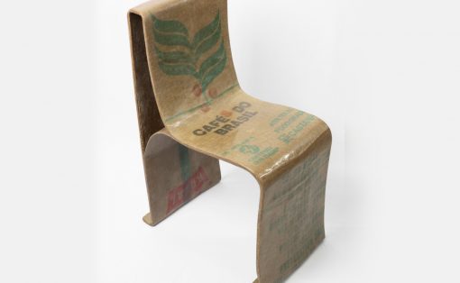 Cardboard chair sculpture made from coffee bag material with a green leaf design and Brazil print, standing on a white backdrop.