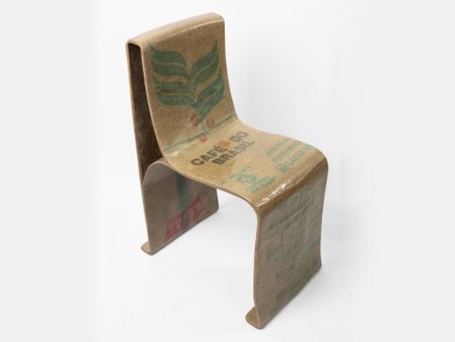 Cardboard chair sculpture made from coffee bag material with a green leaf design and Brazil print, standing on a white backdrop.