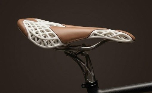 Bike saddle with a white lattice shell and brown leather top mounted on a seat post against a dark background.