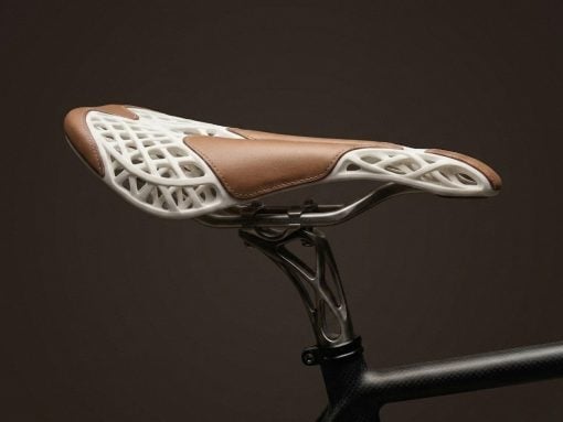 Bike saddle with a white lattice shell and brown leather top mounted on a seat post against a dark background.