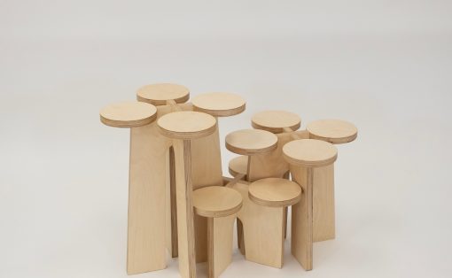 Group of pale wooden stools with round seats arranged in a cluster on a light background.