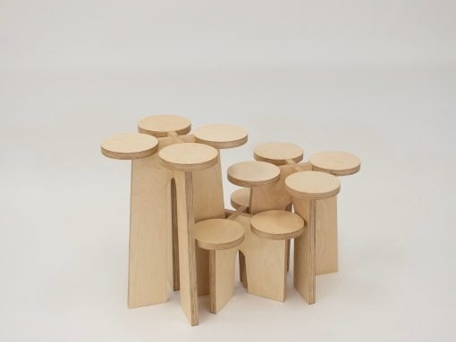 Group of pale wooden stools with round seats arranged in a cluster on a light background.