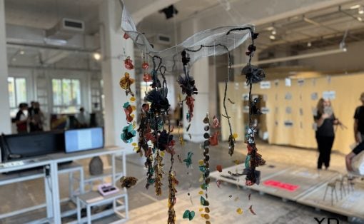 Hanging sculptural piece of colorful glass beads and fabric ribbons suspended from the ceiling in a bright studio space.