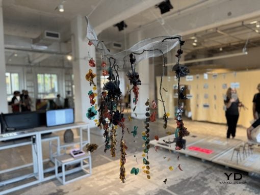 Hanging sculptural piece of colorful glass beads and fabric ribbons suspended from the ceiling in a bright studio space.