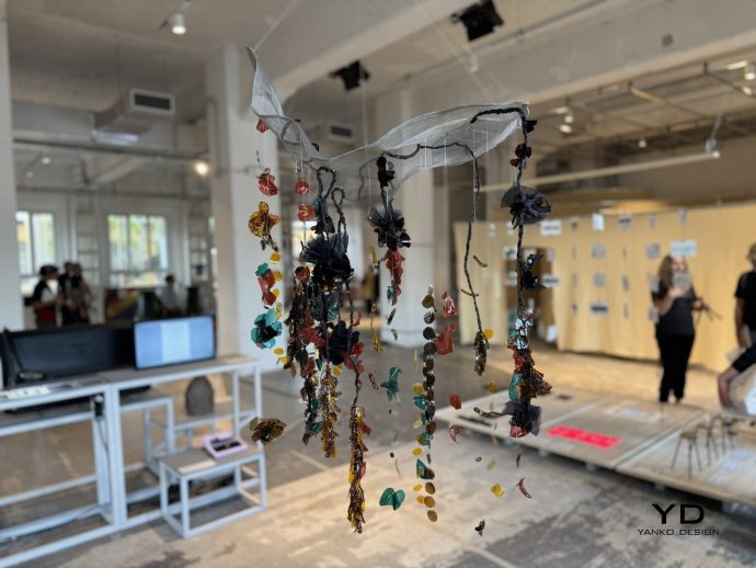 Hanging sculptural piece of colorful glass beads and fabric ribbons suspended from the ceiling in a bright studio space.