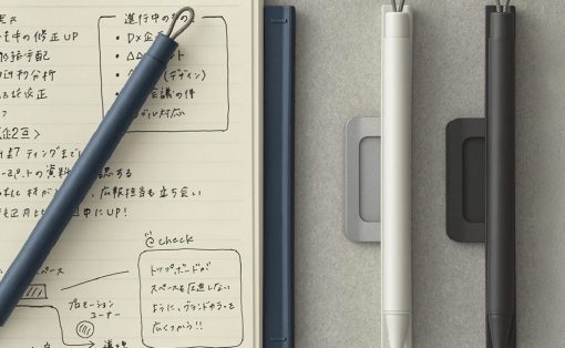 Notebook with handwritten notes in Japanese, a blue pencil resting diagonally across the page, and three pens (white, blue, black) on a gray surface.