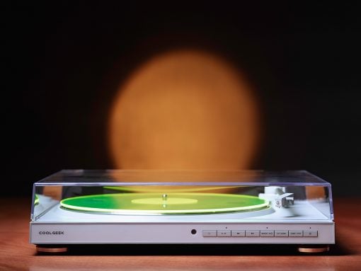 White turntable with a clear lid and a bright green vinyl on a wooden surface, orange blur in the dark background.