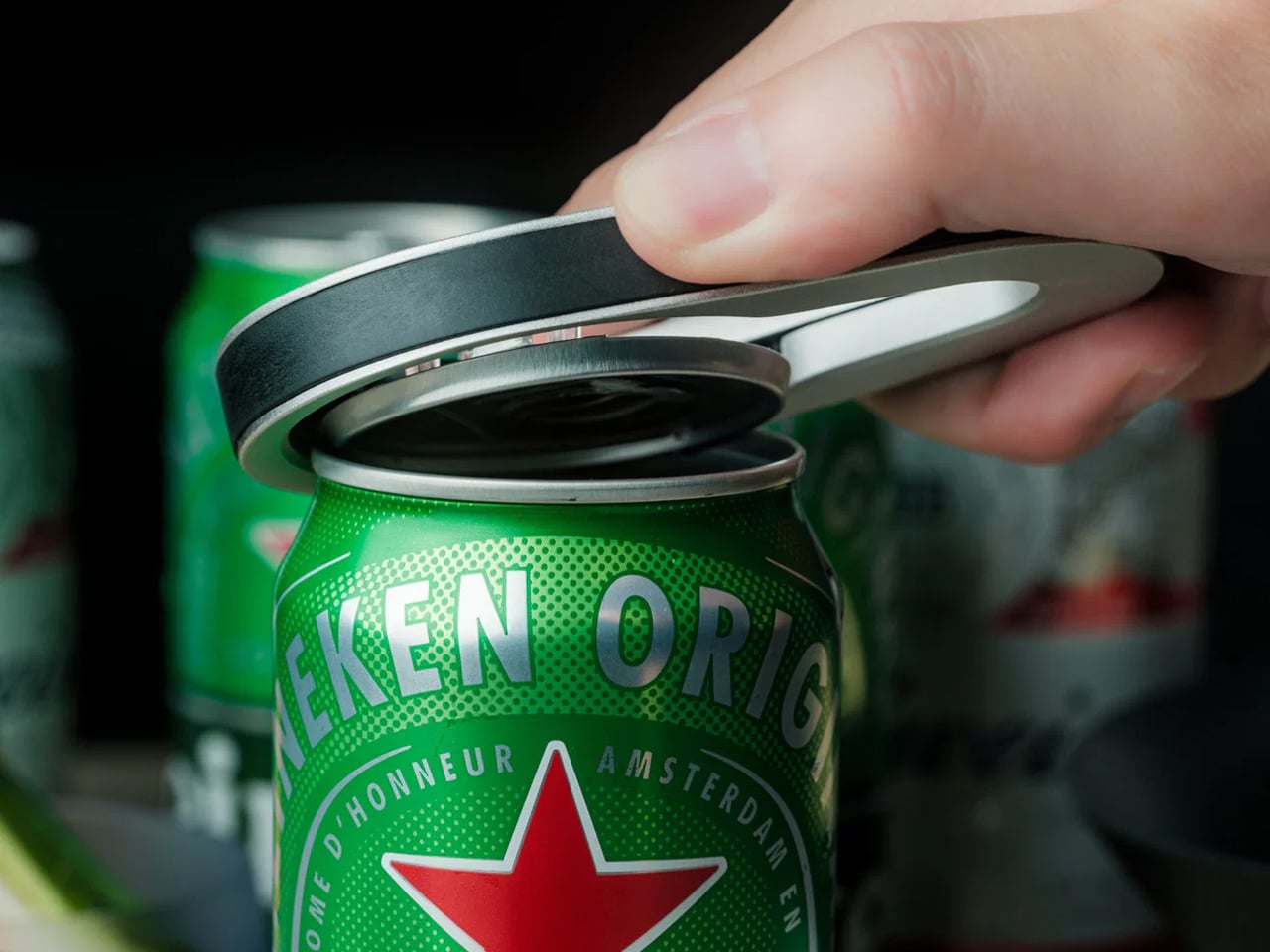 Close-up of a hand opening a green Heineken can with a pull tab, revealing the metal lid edge
