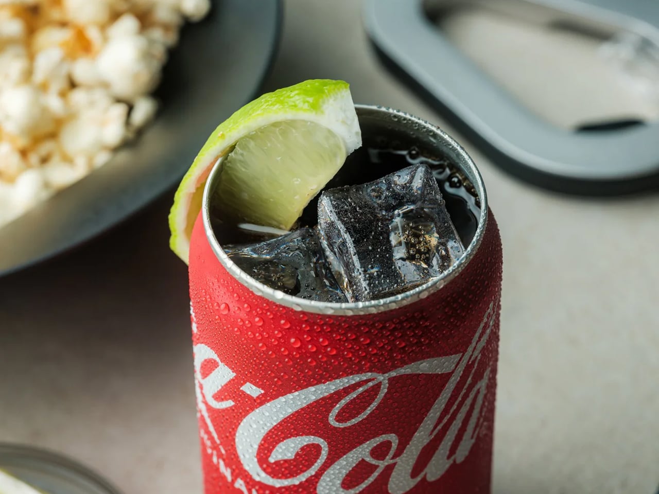 Coca‑Cola can with ice and a lime wedge, condensation on the can.