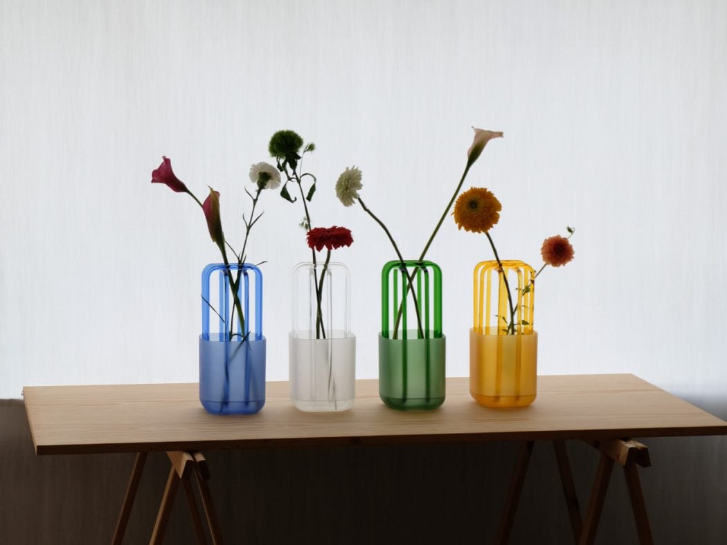 Four colored glass vases with single flower stems on a wooden table.
