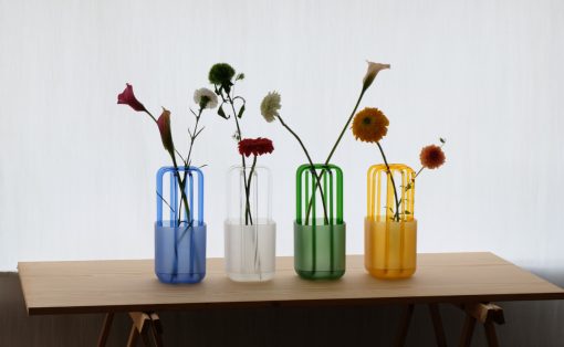 Four colored glass vases with single flower stems on a wooden table.
