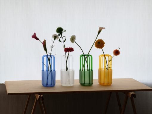 Four colored glass vases with single flower stems on a wooden table.