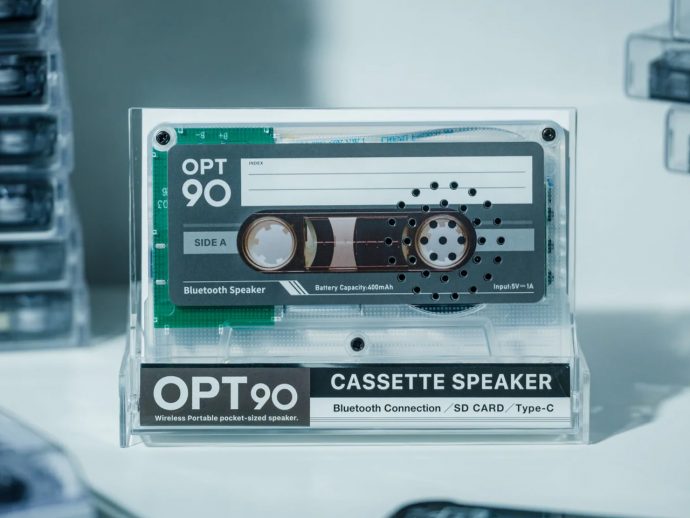Transparent display of an OPT90 cassette speaker in a clear case, with 'CASSette SPEAKER' and 'Bluetooth Connection' labels visible.