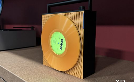 Gold vinyl record mounted on a perforated orange panel with a black base, posed on a wooden cabinet as a design sculpture.
