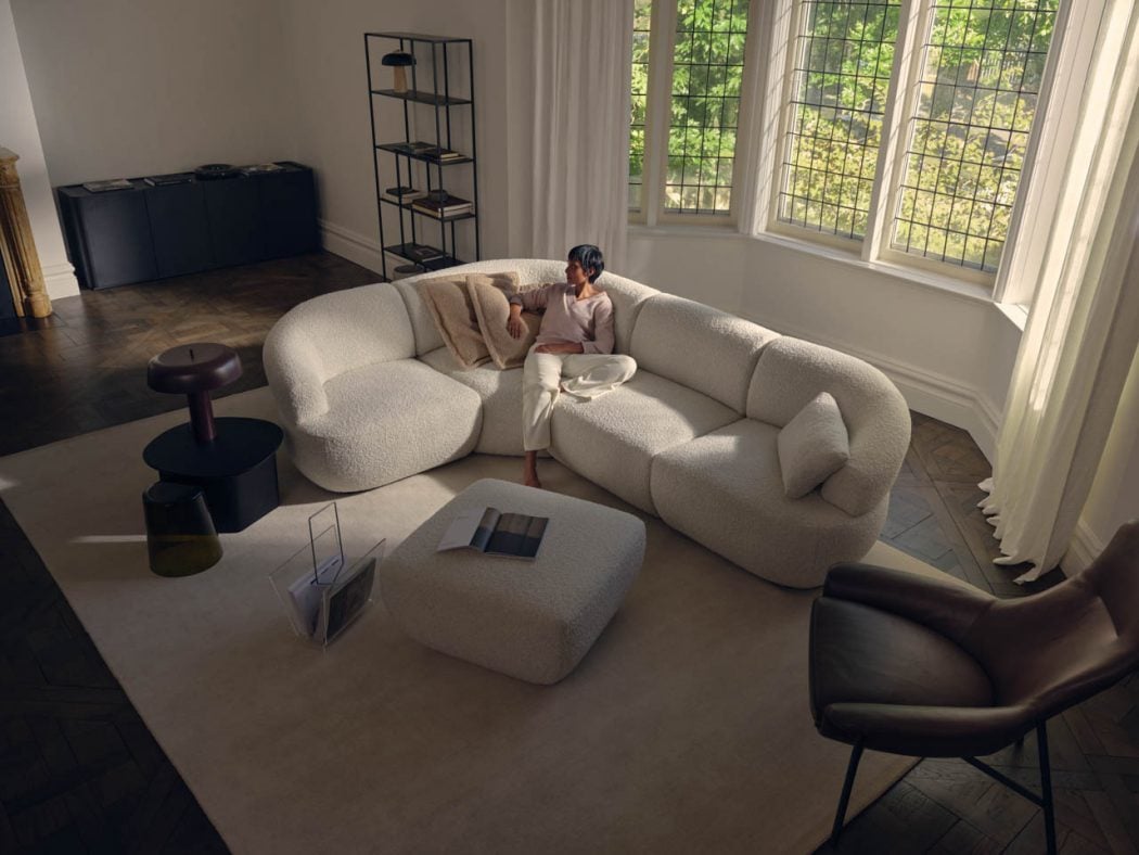 Woman relaxing on a white boucle sectional sofa in a bright living room, with an open magazine on the matching ottoman nearby.