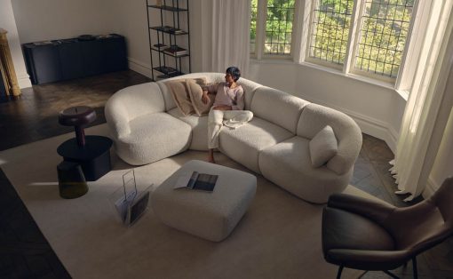 Woman relaxing on a white boucle sectional sofa in a bright living room, with an open magazine on the matching ottoman nearby.