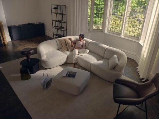 Woman relaxing on a white boucle sectional sofa in a bright living room, with an open magazine on the matching ottoman nearby.