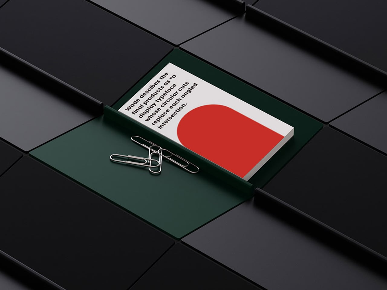 White card with a red curved shape and bold text sits in a green tray, held by paperclips on a dark tiled surface.