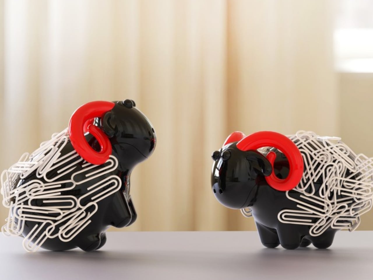 Two black animal figurines with tangled white hair and red headphones facing each other on a table surface.