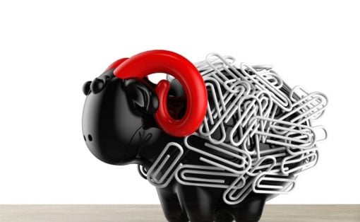 Black piggy bank wrapped in a tangle of silver paperclips with red headphones resting on its head, sitting on a wooden surface.