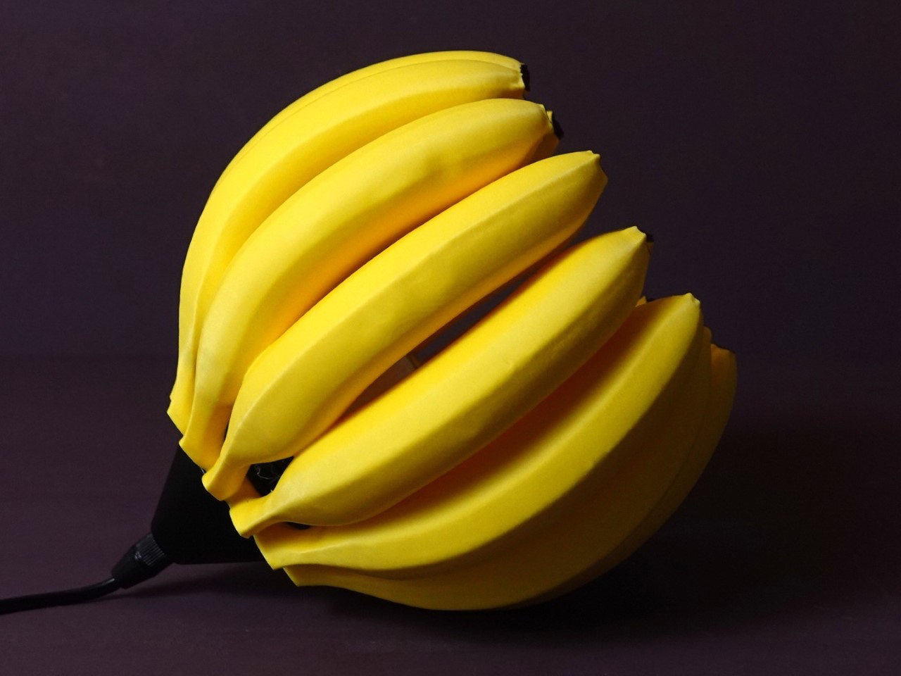Banana-shaped lamp: a cluster of bright yellow bananas forming a lampshade on a dark background with a power cord visible at the base.