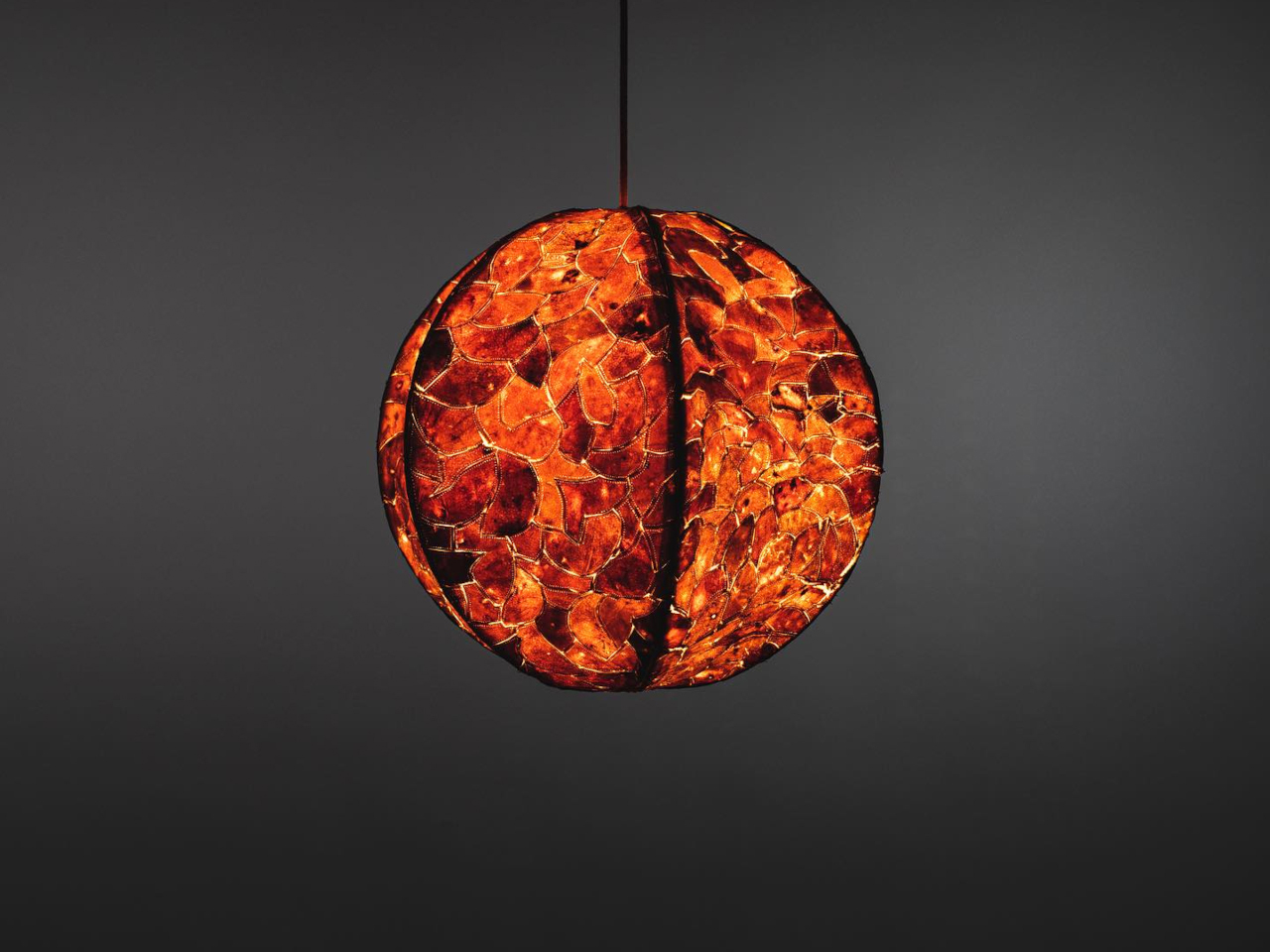 Round orange mosaic pendant lamp hanging from a cord against a dark wall.