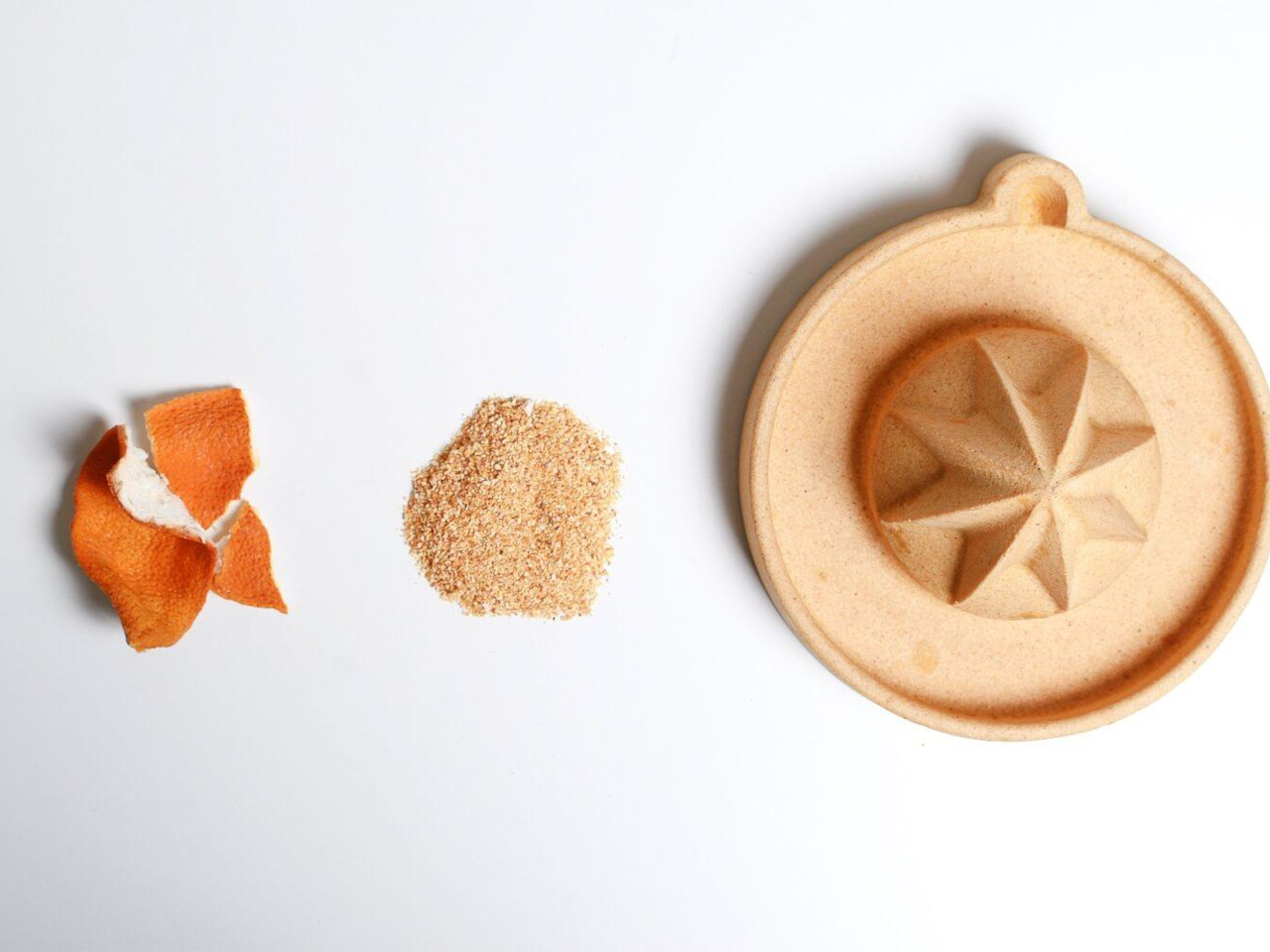 Orange peel pieces and ground zest lined up on a white surface beside a round wooden citrus press/juicer on the right.