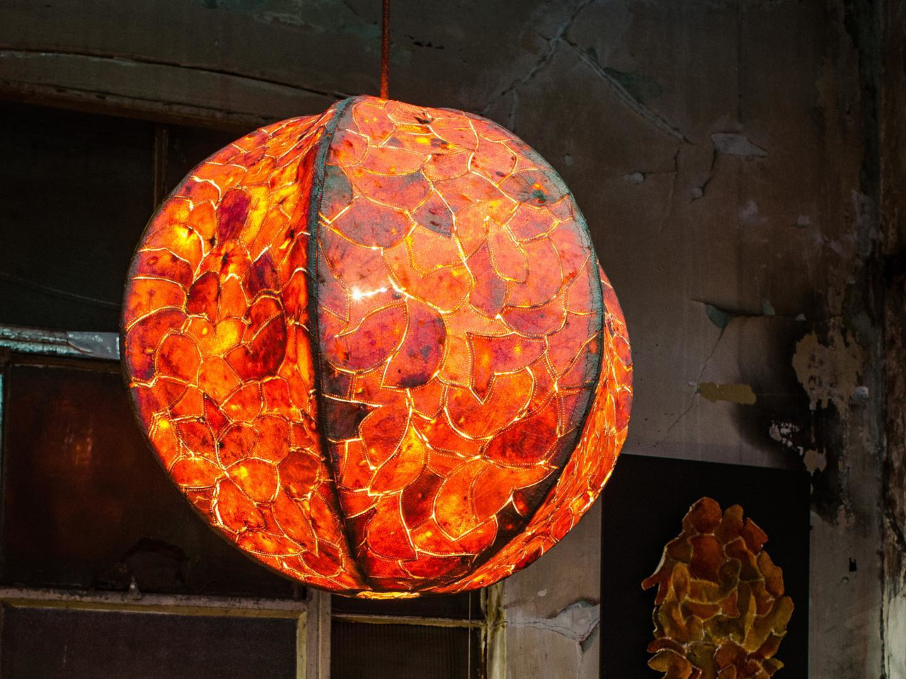 Hanging orange mosaic lantern made of petal-shaped pieces, glowing in a dark room, suspended by a cord.