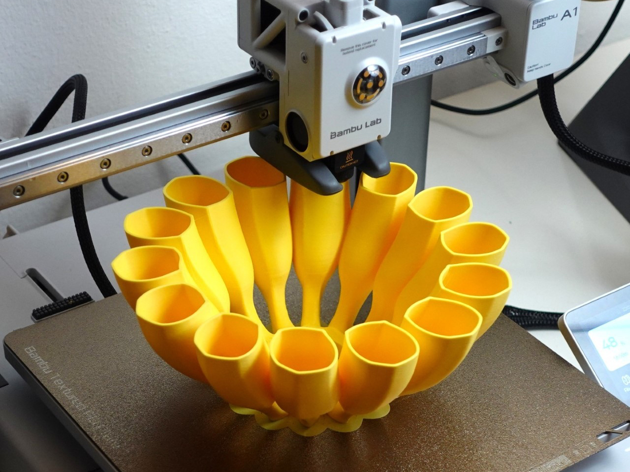 Yellow multi-petal 3D-printed vase being created by a Bambu Lab printer.