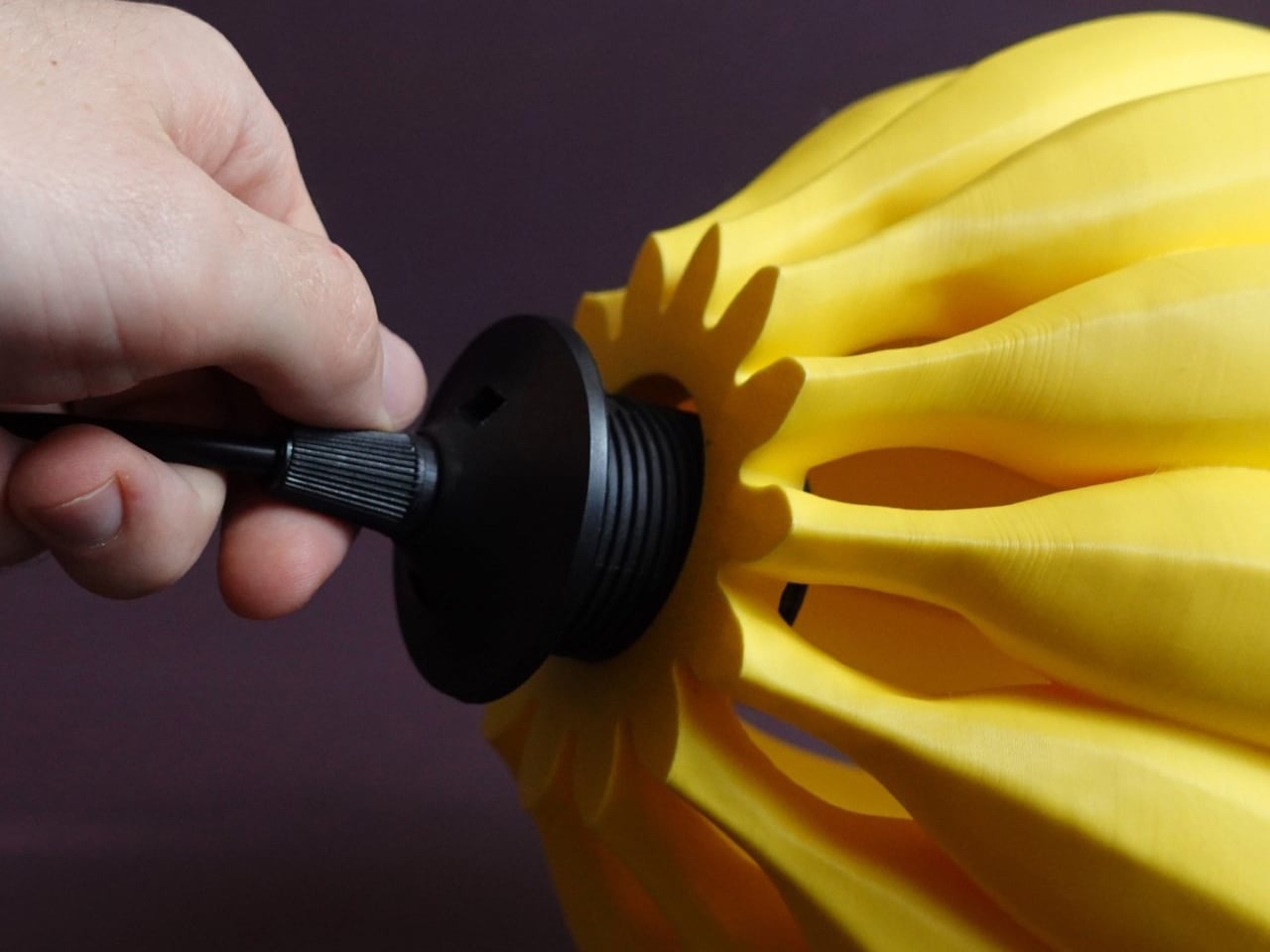 Close-up of a hand turning a black valve on a yellow, petal-like inflatable object.