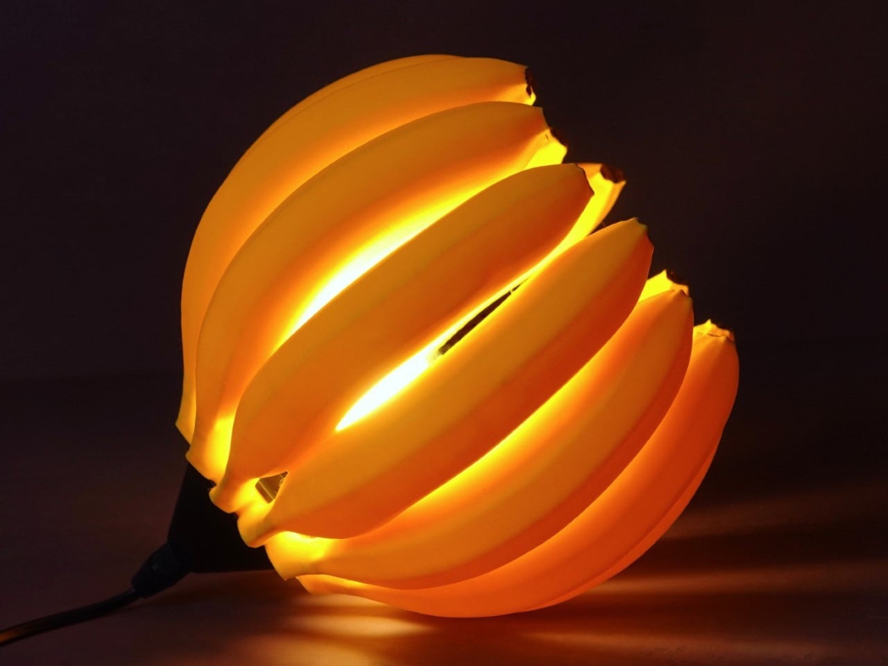 Orange spiral paper lamp lit from inside, glowing on a dark surface.