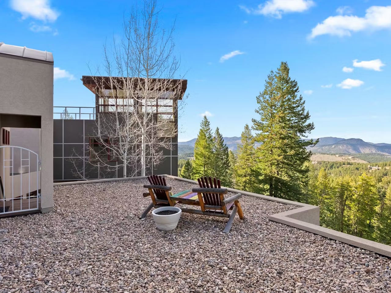 Rooftop patio with two wooden Adirondack chairs and a small table, overlooking trees and distant mountains.