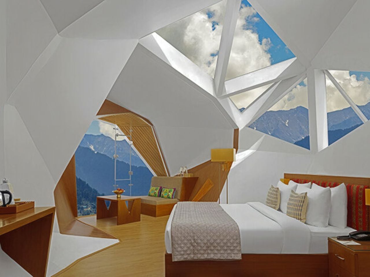 Modern hotel room with geometric white walls, a wooden bed and seating area, and panoramic mountain view through angular windows
