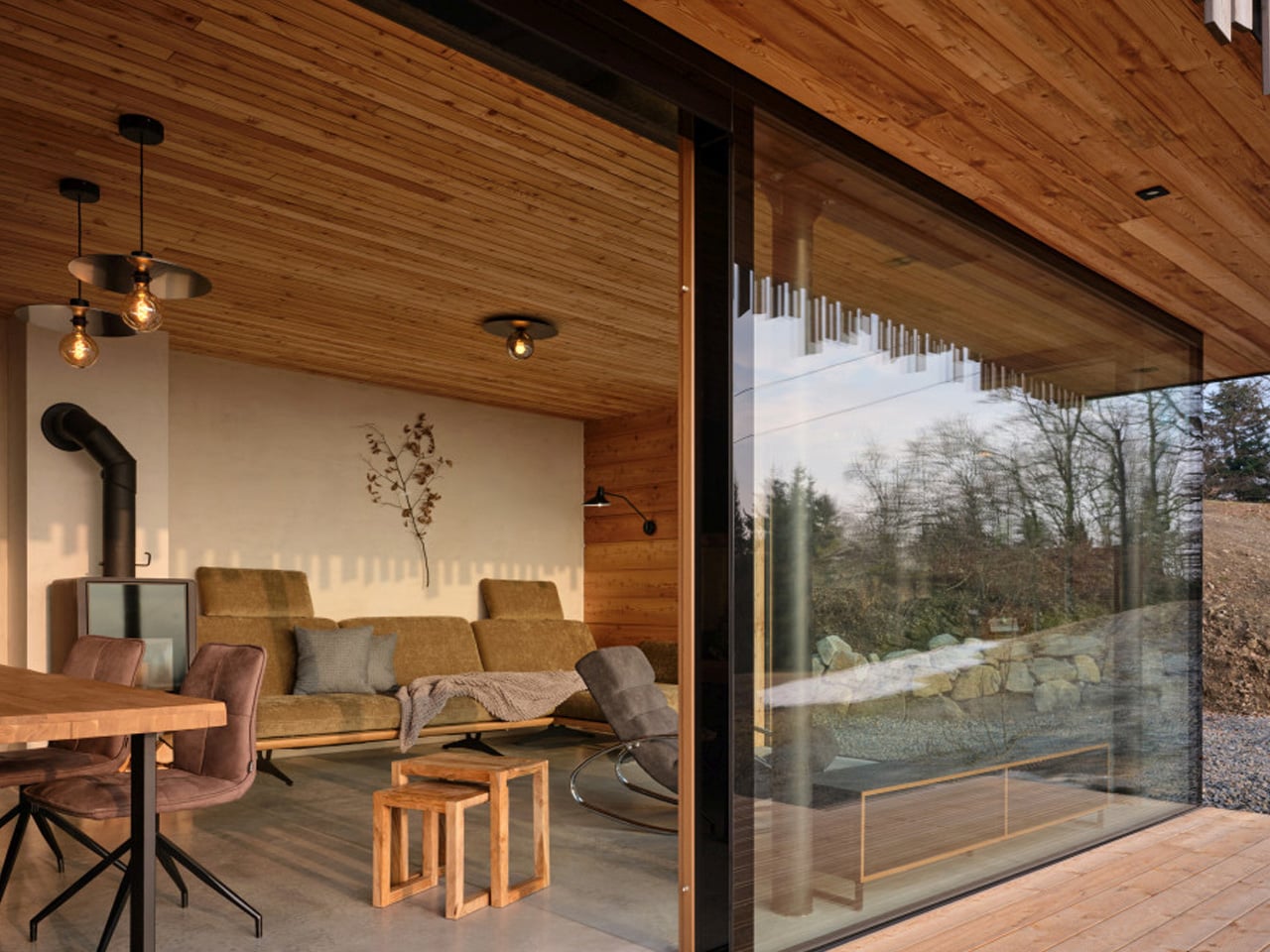 Modern living room with wood ceiling, beige sofa, and a large glass wall opening to an outdoor area.