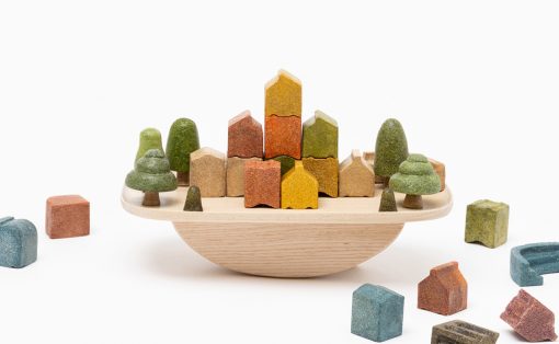 Wooden toy city: colorful houses and trees arranged on a round wooden tray, with extra blocks around it.