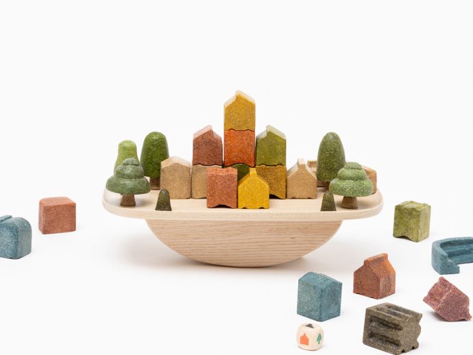 Wooden toy city: colorful houses and trees arranged on a round wooden tray, with extra blocks around it.