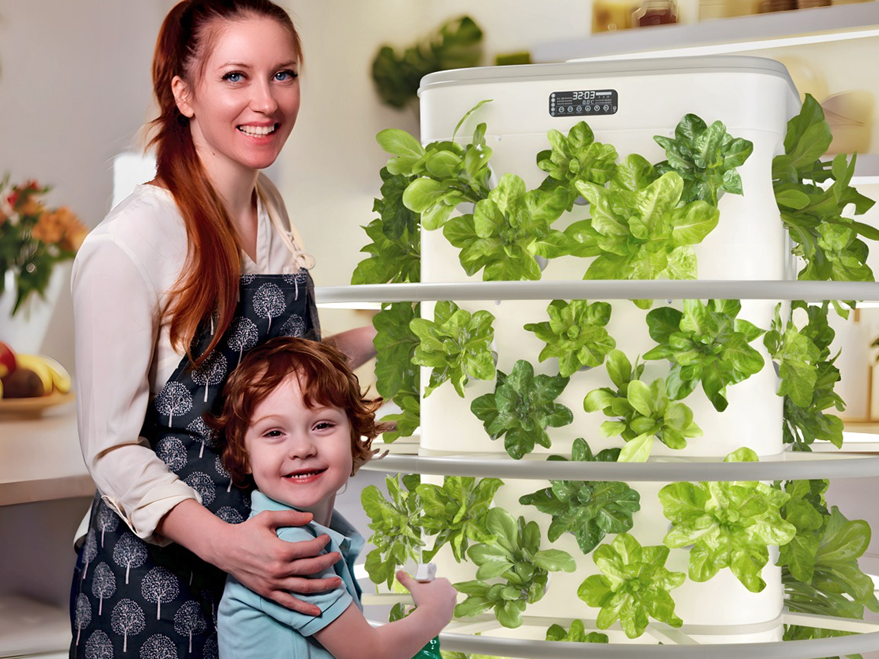Smiling woman in an apron stands beside a white vertical planter filled with green leafy plants (lettuce).