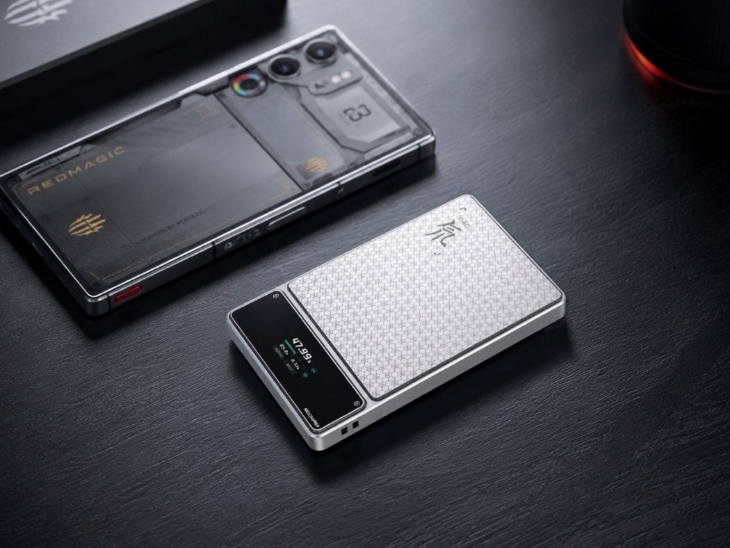 Two modern smartphones on a dark wooden desk, one with a textured white honeycomb back and a small display, the other with a clear protective case revealing its internals and camera array.