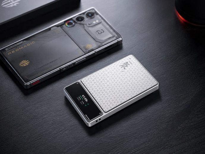 Two modern smartphones on a dark wooden desk, one with a textured white honeycomb back and a small display, the other with a clear protective case revealing its internals and camera array.