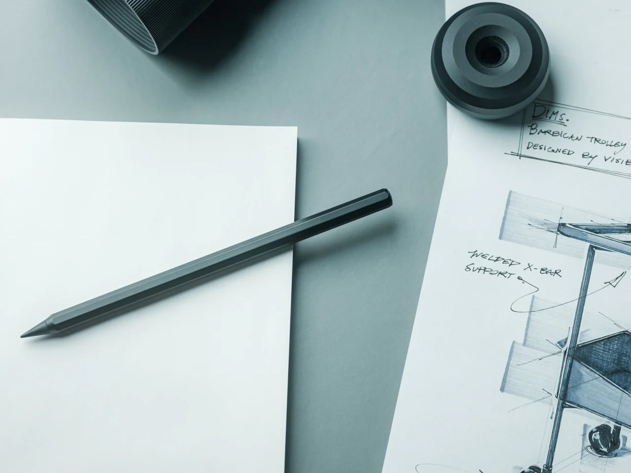 Pencil rests on white paper beside design sketches and a roll of tape on a light desk surface
