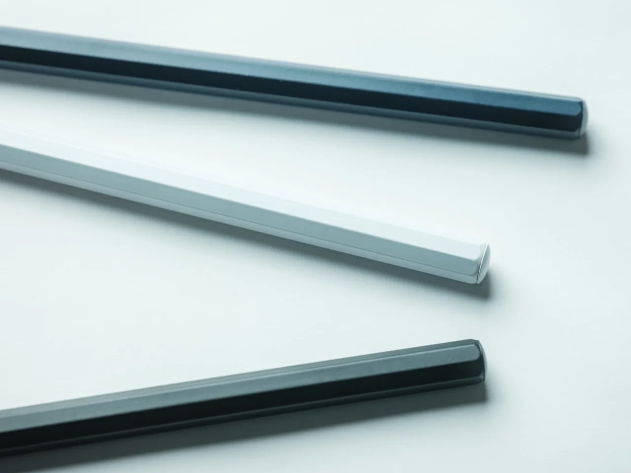 Three metal rods with rounded ends lie diagonally on a white surface (two dark gray, one light gray).