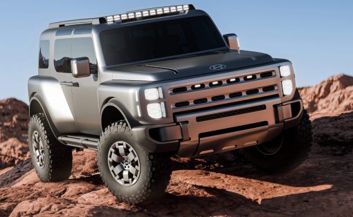 Silver rugged SUV with a roof rack and oversized tires navigating rocky desert terrain under a clear blue sky, front-right angle view.