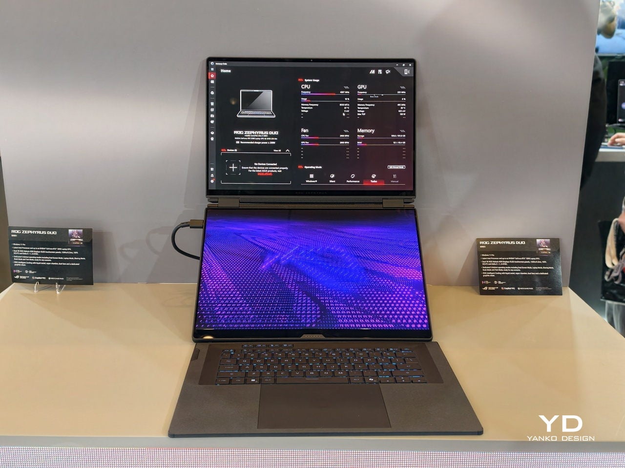 Dual-screen laptop on a showroom table; main keyboard visible and purple-pattern display on the lower screen, upper screen showing software UI.