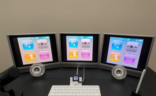 Three-monitor computer desk setup displaying iTunes app icons on all screens, with a microphone on the left and a white keyboard in front.